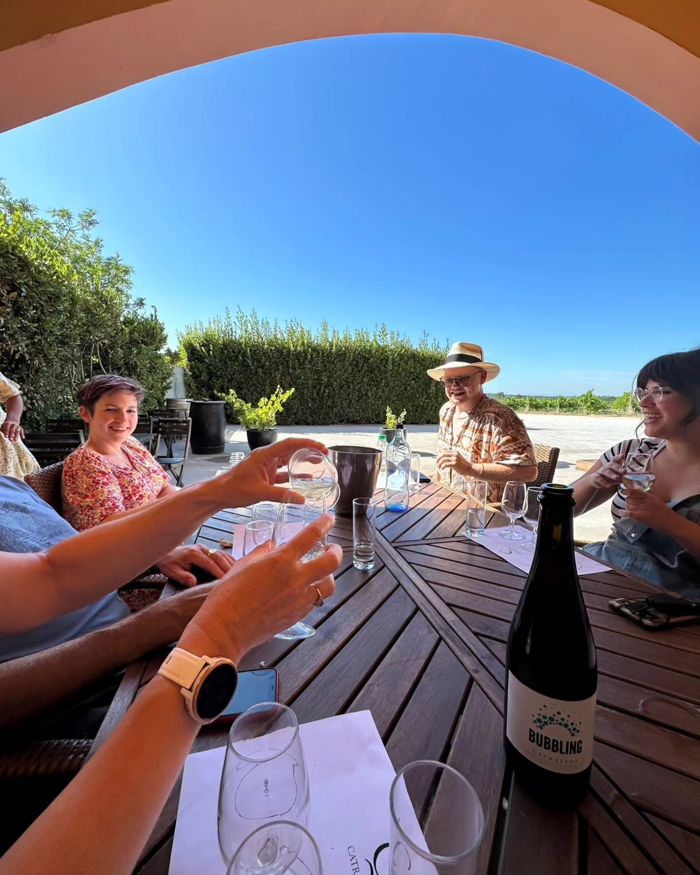 Friends raising Portuguese wine glasses together beneath a shaded stone arch.